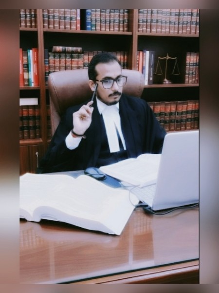 Founder in robes at a desk in front of a wall of law reports