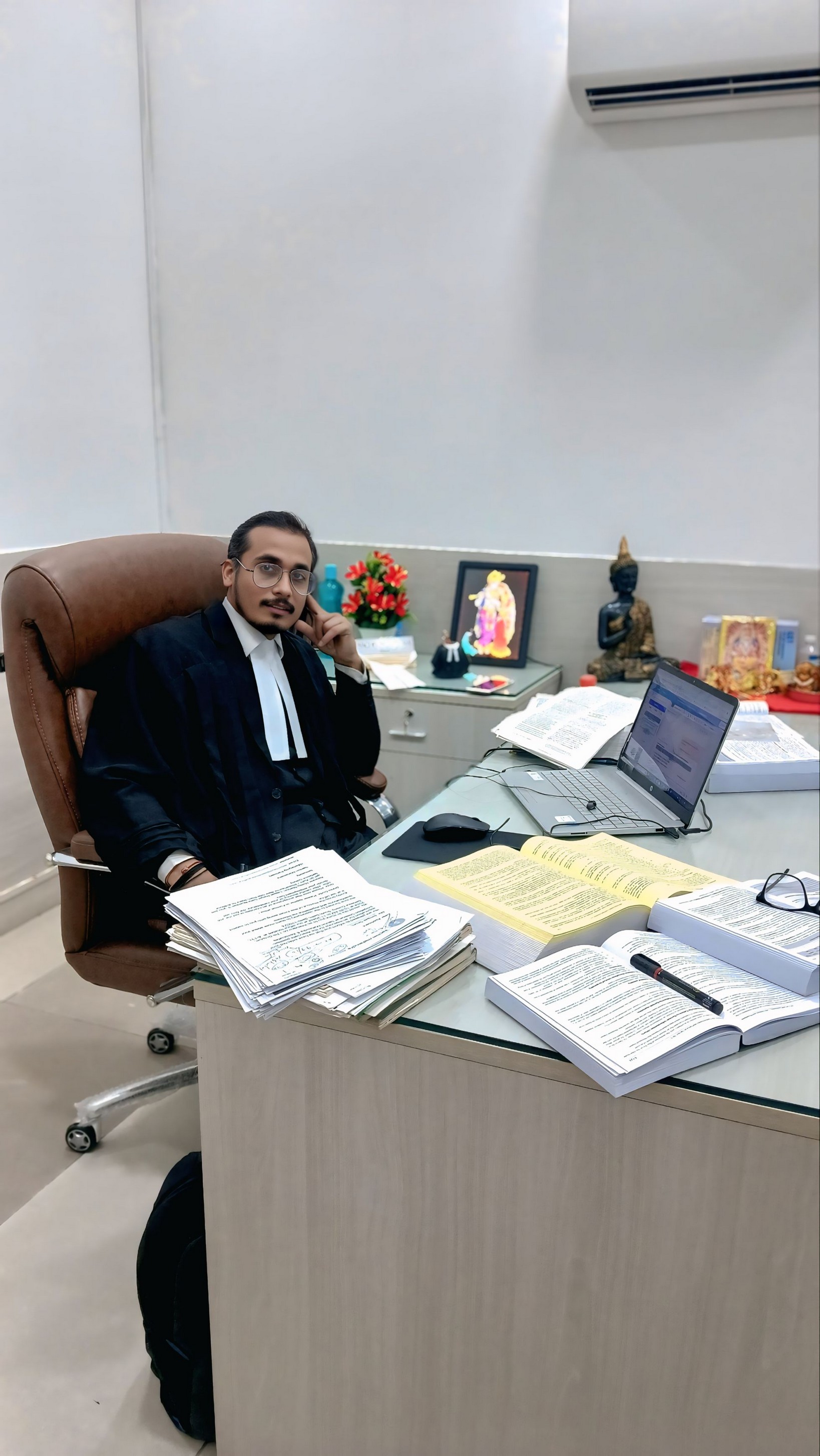 Founder in advocate robes at his office cabin desk with books and a laptop